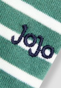 Zöld és fehér csíkos szövet, puha tapintással, sötétkék cérnával hímzett "JoJo" felirattal. A közeli nézet kiemeli a részleteket és a varratokat.