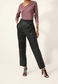 Sudenroosa pitkähihainen paita, jossa on vinoraitasuunnittelu. Mustat tekonahkapöksyt, joissa on näkyvät saumat ja elastinen vyötärö. Ristiriipuksilla varustetut mustat korkokengät.