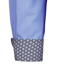 Polsino di camicia azzurro chiaro con una fascia contrastante blu scuro che presenta un motivo circolare ripetitivo in bianco e azzurro chiaro. Design strutturato.