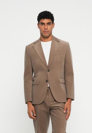 Rjav kordurojski suit s slim fit krojem, blazerjem z enim gumbom, zarezami in ujemajočimi hlačami, nošenim preko bele majice.