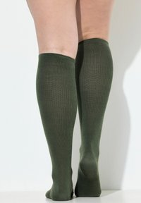 Calze al ginocchio color verde oliva con una texture a costine, materiale liscio e senza motivi o componenti visibili. Le fibre sembrano morbide ed elastiche.
