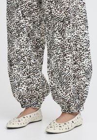 Pantalons à motifs noir et blanc avec des poignets élastiques, associés à des ballerines crème avec des clous décoratifs en argent et un bout arrondi.