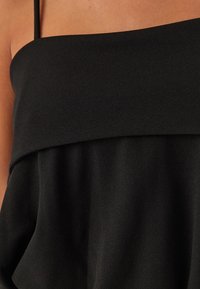 Top nero senza maniche con una vestibilità ampia, caratterizzato da un design drappeggiato e una consistenza morbida. Il materiale appare leggero e liscio.