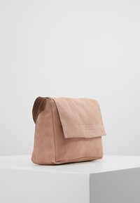 Růžová semišová taška s klopou, která má hladký povrch a minimalistický design. Na přední straně je jemný šev.