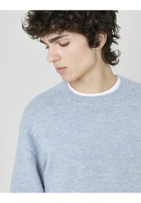 Pull tricot léger bleu clair avec un col rond, fabriqué à partir de matériaux doux, présentant une finition légèrement texturée et une coupe standard.