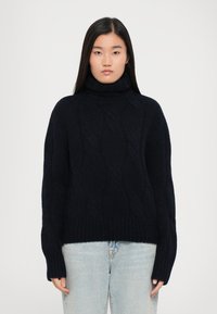 Dunkelblaues Strick-Turtleneck mit Rippbündchen und -saum. Das Material scheint weich und strukturiert zu sein, geeignet für kältere Wetterbedingungen.