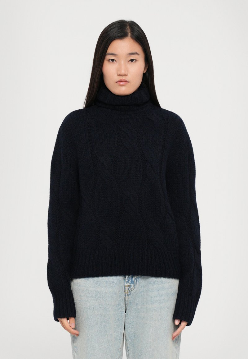 Dunkelblaues Strick-Turtleneck mit Rippbündchen und -saum. Das Material scheint weich und strukturiert zu sein, geeignet für kältere Wetterbedingungen.