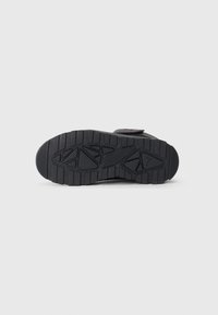 Zwarte sneakersole van structuur rubber, met een profielpatroon voor grip en een afgeronde vorm, ontworpen voor duurzaamheid en stabiliteit.