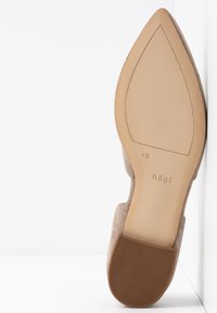 Chaussure en daim beige avec bout pointu, semelle extérieure en caoutchouc et design minimaliste. Comprend un logo embossé et une silhouette élégante.