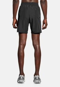 Czarne sportowe szorty z elastycznym pasem i kieszenią boczną, wykonane z lekkiego materiału, noszone z szarymi trampkami.