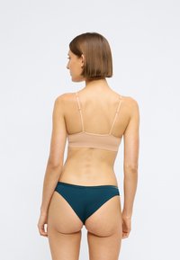 Hladká, bezšvová podprsenka bez výztuže s nastavitelnými ramínky v nude barvě spárovaná s tmavě modrými nízko pasovými kalhotkami, obojí vyrobené z jemné, hladké látky.