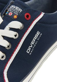 Granatowe płócienne trampki z białymi sznurówkami, czerwono-białymi paskami i srebrnymi oczkami. Zawierają tekst logo oraz branding klubu żeglarskiego.