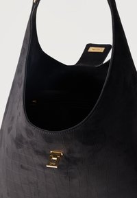 Μαύρη υφασμάτινη δερμάτινη τσάντα με χρυσό κούμπωμα και ανοιχτό επάνω μέρος που αποκαλύπτει μαύρο εσωτερικό και μικρή εσωτερική τσέπη.