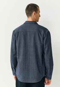 Cămașă lungă albastru închis, dintr-un material texturat, cu guler ascuns și tiv, având un model discret în zig-zag.
