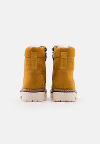 Stivaletti alla caviglia in suede giallo con fodera in pelliccia bianca, suola spessa bianca e un piccolo anello sul retro per indossarli facilmente.