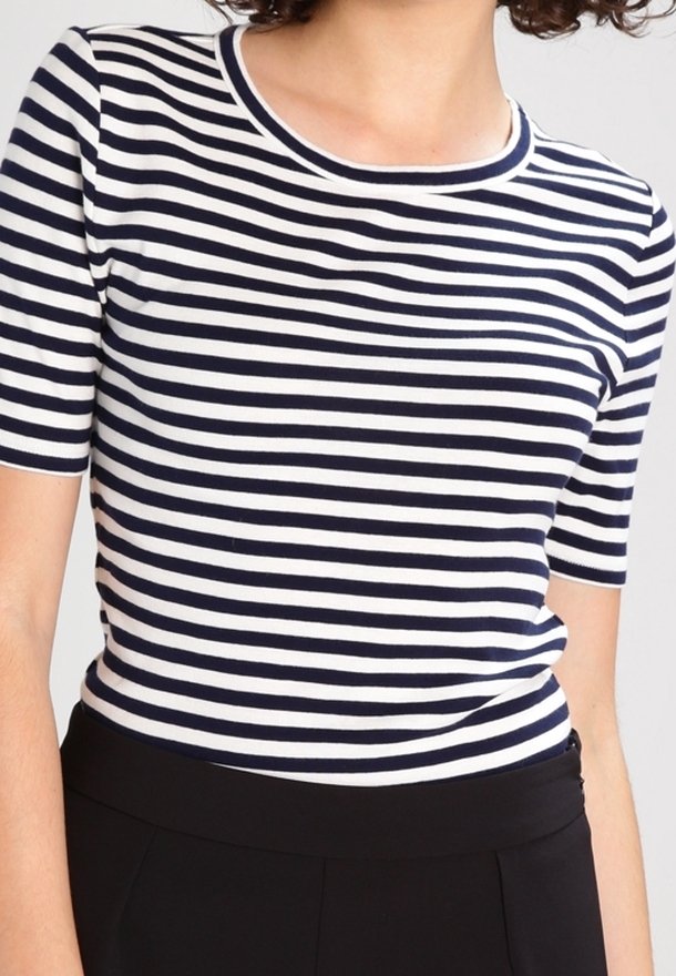 Kobieta w granatowo-białym topie w poziome paski z krótkim rękawem, włożona do wysokich czarnych spodni.