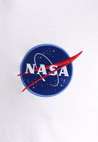 Tissu blanc avec un logo NASA bleu, comprenant une courbe rouge et des lignes d'orbite blanches avec des étoiles.