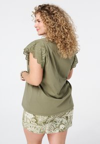 Haut court vert olive avec des détails en dentelle brodée sur l'épaule et un short à motifs vert et crème, présentant un design fluide.