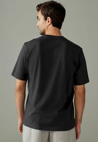Camiseta de algodón negra de manga corta, con un escote redondo y un corte holgado, vista desde la parte de atrás. Textura suave. Sin patrones.