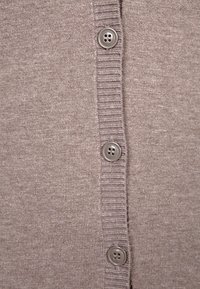 Jasnobrązowy kardigan z fakturowanej tkaniny, z rzędem pięciu szarych guzików na listwie oraz prążkowanymi detalami na krawędziach.