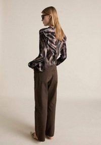 Printed long-sleeve shirt in shades of grey and brown, paired with brown wide-leg trousers; model seen from the back, wearing sunglasses.