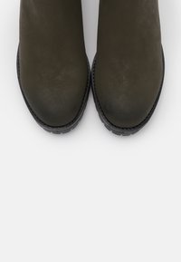 Botas de tobillo verde oscuro hechas de cuero suave con puntera redondeada y suela de goma negra texturizada. Diseño minimalista, sin hardware visible.