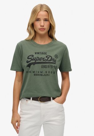 T-shirt en coton vert à manches courtes, décolleté rond, avec un imprimé graphique noir vintage arborant le texte et le logo "SuperDry".