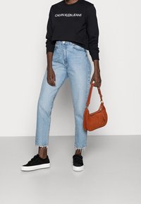 Černá mikina s textem "CALVIN KLEIN JEANS", světle modré džíny s vysokým pasem, černé tenisky a oranžová kožená kabelka s krátkým popruhem.