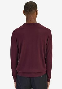 Burgundy stickad sweatshirt med lång ärm, rund halsringning och ribbade manschetter i en avslappnad passform. Texturen verkar mjuk och slät.