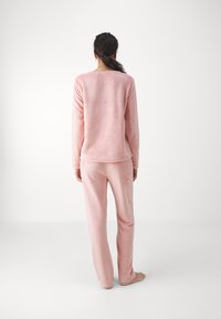 Conjunto de pijama de forro polar en rosa claro, que incluye una camiseta de manga larga y pantalones. Textura suave, ajuste relajado y diseño simple sin adornos.