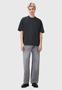 Sort bomulds t-shirt med en afslappet pasform, der har rund hals og korte ærmer. Sammen med lysegrå bukser med brede ben og sorte sko.