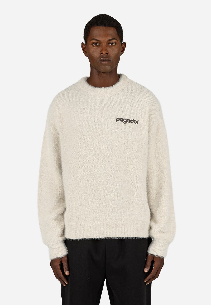 Svetlo bež pulover z mehkobo in puhastim materialom. Ima okroglo ovratnico in dolge rokave. Na prsih je izvezen napis "Pagador" v temni nitki.