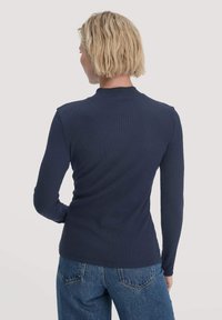 Marineblaues, langärmeliges, geripptes Oberteil mit taillierter Passform, Rundhalsausschnitt und weichem Material, kombiniert mit leicht verwaschenen blauen Jeans.