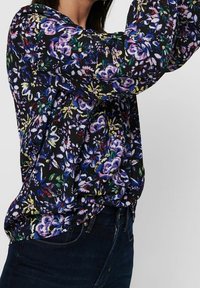 Blusa floreale con sfondo nero e variopinte fantasie di fiori. Maniche lunghe con vestibilità ampia e tessuto morbido e leggero.
