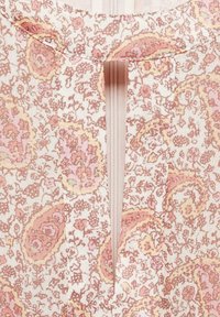 Detailní záběr béžové a růžové látky s paisley vzorem, s částečně viditelným skrytým vertikálním zipem ve středu.
