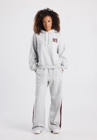 Gray hooded sweatshirt with red "89" graphic, paired with gray sweatpants featuring maroon side stripes, made from soft fabric.