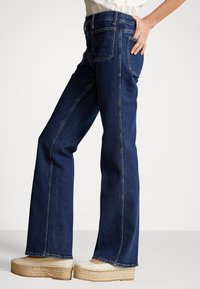 Mörkblå jeans med utsvängda ben i denim, med hög midja, design med fem fickor och synliga sömmar, kombinerade med beige platåespadrillos.