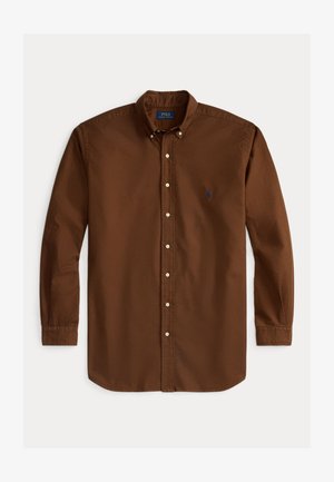 Camisa de manga larga marrón, tipo botón, hecha de algodón, con un cuello clásico, botones blancos y un pequeño logo azul en el lado izquierdo del pecho.