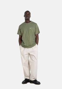 Olive green cotton t-shirt with short sleeves and a crew neck, paired with beige wide-leg trousers and black shoes. Simple design, no patterns.