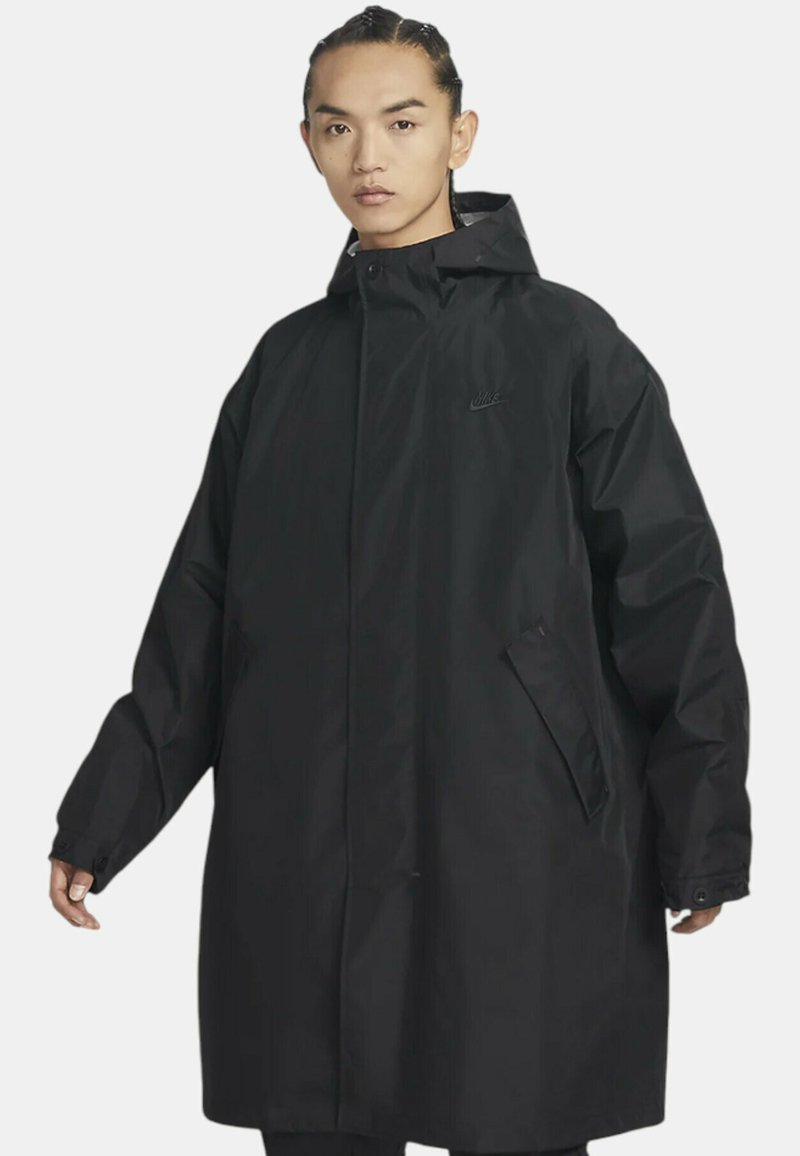 Cappotto impermeabile nero con colletto alto, maniche lunghe e vestibilità morbida. Presenta una zip frontale, tasche laterali e un sottile logo decorativo.