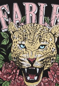 Černé grafické tričko s detailním motivem leopardí tváře v žluté barvě a modrýma očima, obklopené zelenými listy a růžovými růžemi, s tučným textem nahoře.