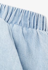 Το γαλάζιο τζιν ύφασμα διαθέτει υφή ύφανσης, με μια σούρα ελαστική μέση, που αναδεικνύει μαλακά και casual στοιχεία σχεδιασμού.