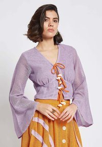Lavender mesh blouse with bell sleeves and orange drawstring, featuring white decorative beads down the front, paired with a textured yellow skirt.
