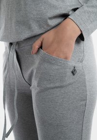 Grijze katoenen joggingbroek met een trekkoord in de taille, zijzakken en een klein merklabel op de zak. Zachte textuur met een gladde afwerking.