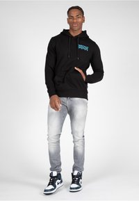 Sudadera negra con capucha y gráfico azul "WRONG FRIENDS", combinada con jeans gris claro y zapatillas de caña alta en blanco y negro.