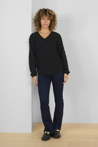 Maglione nero a maglia con scollo a V e un motivo testurizzato, abbinato a jeans svasati blu scuro e scarpe nere con dettagli dorati.