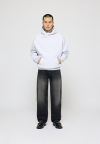 Hanorac gri cu gluga, cu buzunare frontale, asortat cu blugi gri închis, cu croială largă, și mocasini negri. Design simplu și siluetă relaxată.