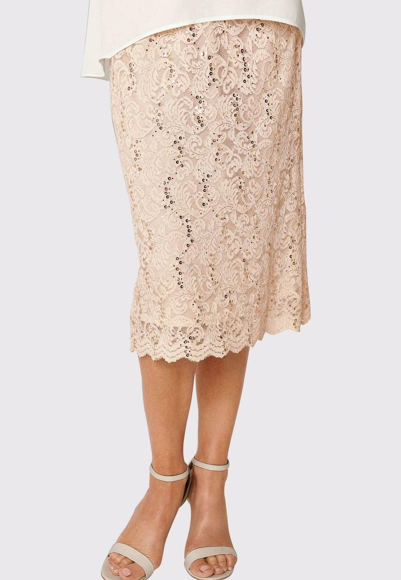 Bügelrock aus Spitze in hellbeige mit Blumenmuster und gewelltem Saum. Kombiniert mit hellfarbigen, hohen Sandalen.
