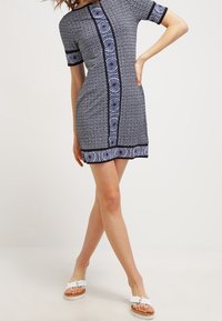 Kortärmad klänning i marinblått med vitt geometriskt mönster. Har rund halsringning, figurnära passform och kontrasterande kant vid fållen.