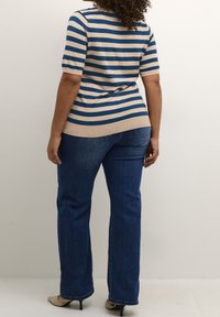 Blå og beige stribet striktrøje med korte ærmer, parret med mørkeblå denim jeans. Trøjen har en tætsiddende silhuet og ribbet kant.